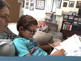 boy sitting in woman's lap in living room and working in a workbook